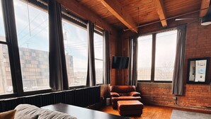 Una sala de estar moderna con sofá, sillones de cuero, televisor de pantalla plana y ventanas grandes con cortinas.