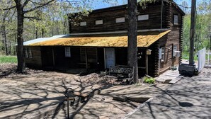 A rustic log cabin with a covered porch, a small front yard, and a wooden bench.