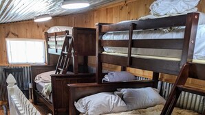 A bunk bed room with a wooden ladder, a desk, and a white railing.