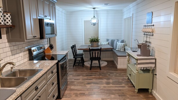 A kitchen with a central island, wooden flooring, and white cabinetry. - The Corner Cottage with Private Fishing Pond (Roland)