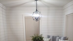 A dining area with a wooden table, black chairs, a round table, a bench with cushions, a potted plant, and a hanging light fixture. - The Corner Cottage with Private Fishing Pond (Roland)