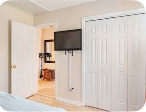 A room with a television mounted on the wall, a white door, and a wooden floor.