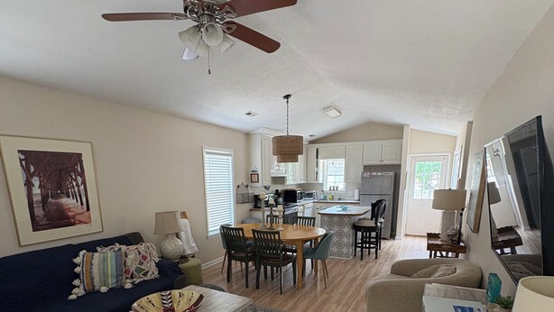 A spacious living room with a ceiling fan, a dining area, and a kitchen in the background.