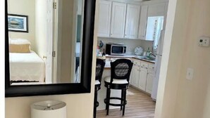 A hallway leading to a bedroom with a large mirror and a bedside table with a lamp.