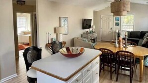 A modern kitchen with white cabinetry, a central island, and a dining area with wooden chairs and a table.