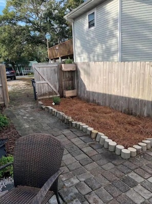 Un jardin à l’arrière de la maison, délimité par une clôture en bois, avec un parterre surélevé recouvert de paillis et un chemin pavé.