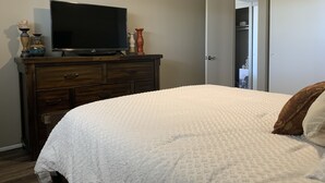 Un dormitorio con cama, un tocador con televisor y una puerta que da a un armario.