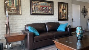 Una sala de estar con un sofá de cuero marrón, cojines color turquesa, una mesa de centro de madera y dos cuadros en la pared.