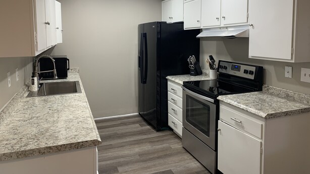Una cocina compacta con gabinetes blancos, un refrigerador negro, estufa y pileta.