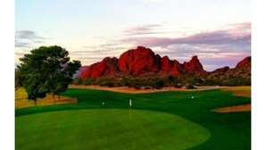 Un campo da golf con una bandiera, alberi e formazioni rocciose rosse sullo sfondo.
