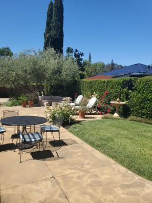Enjoy dining or socializing in this serene outdoor space surrounded by a tall tree and neatly trimmed hedge.