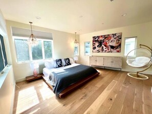 Un dormitorio moderno con una cama grande, una silla colgante y un cuadro abstracto de gran tamaño en la pared.