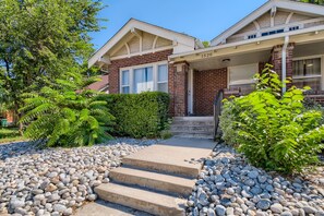 Steps lead to the front door of this two-story residence, surrounded by lush greenery and a gravel pathway.