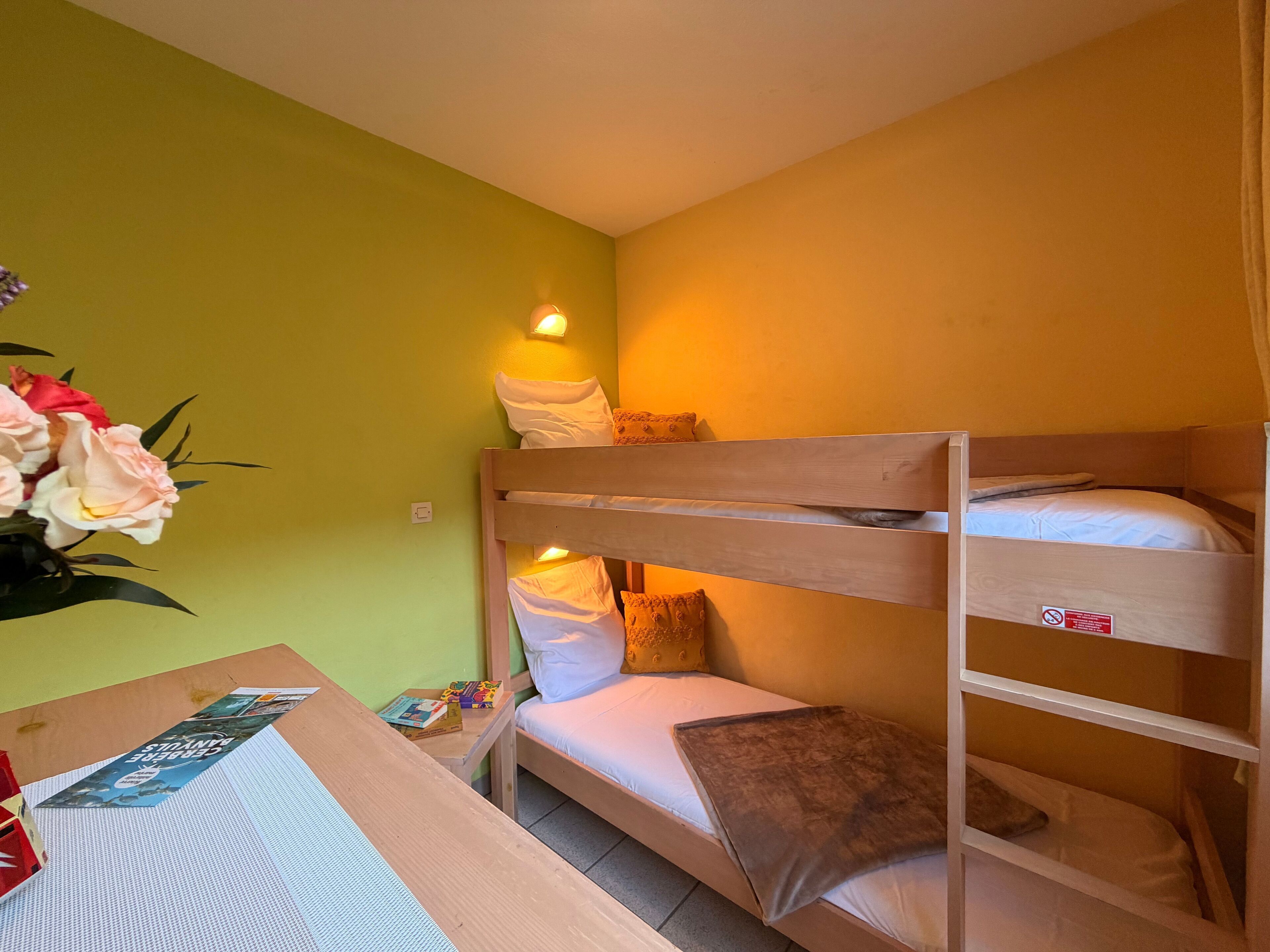 A bunk bed room with a green wall, a table with books, and a vase of flowers.