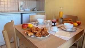 Ein Frühstückstisch mit Croissants, Früchten und Getränken in einer Küchenecke.