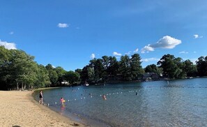 A lake with people swimming and walking on the shore, surrounded by trees and a building in the background. - Beautiful and modern 3 Bedroom 2 full BR. (Marlborough)