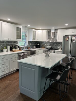 A modern kitchen with white cabinets, a central island, stainless steel appliances, and a black bar stool. - Beautiful and modern 3 Bedroom 2 full BR. (Marlborough)