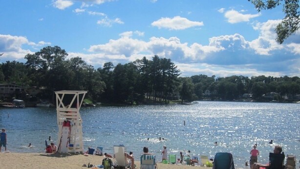 A beach with a lifeguard tower, people sunbathing, and a lake.