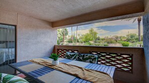 A balcony with a view of a landscaped garden, a table with a plant, and a bed with a patterned headboard. - Epic Biltmore 103 (Phoenix)