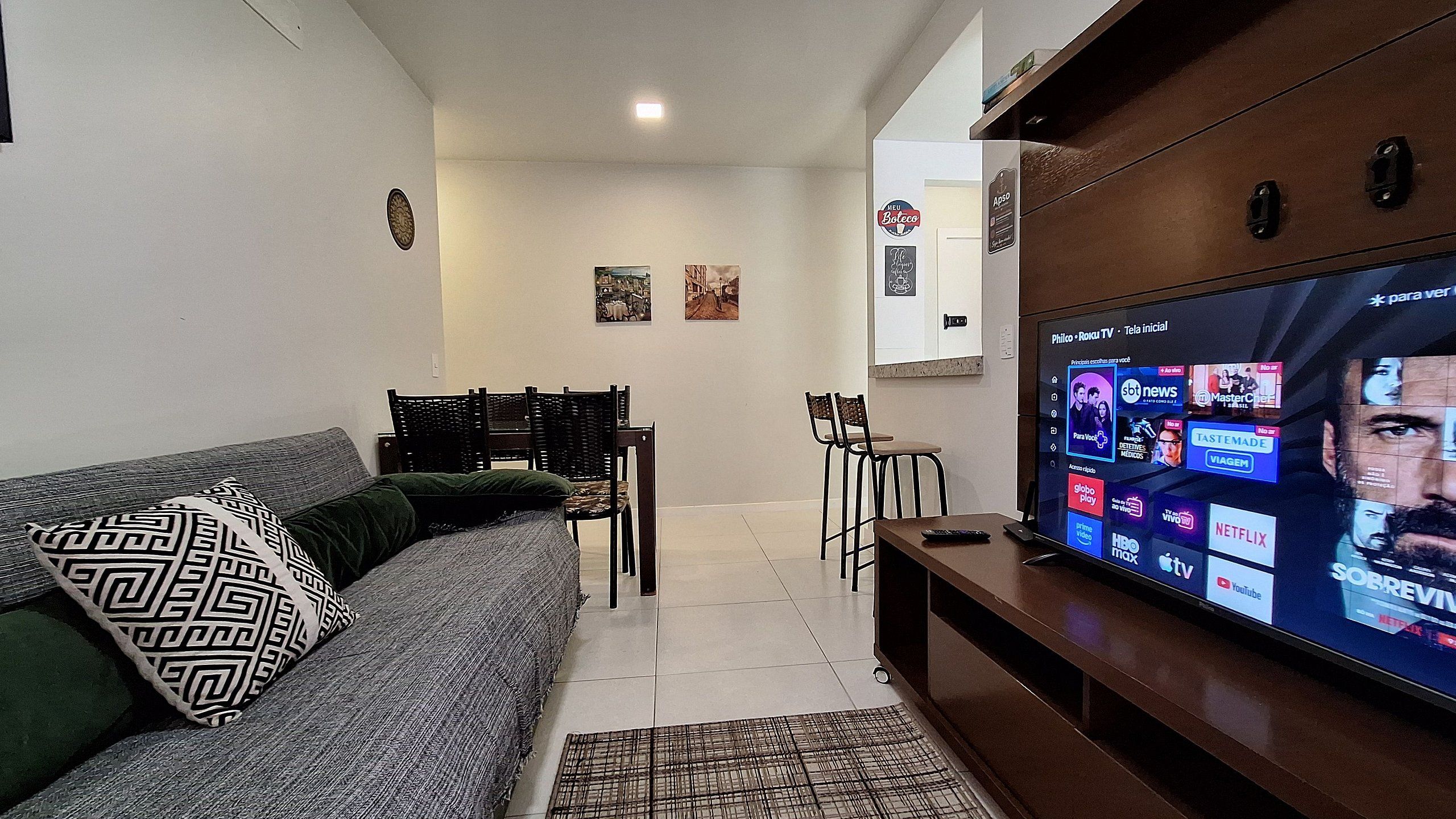 Un salon avec un canapé, des fauteuils, un téléviseur et une étagère fixée au mur.