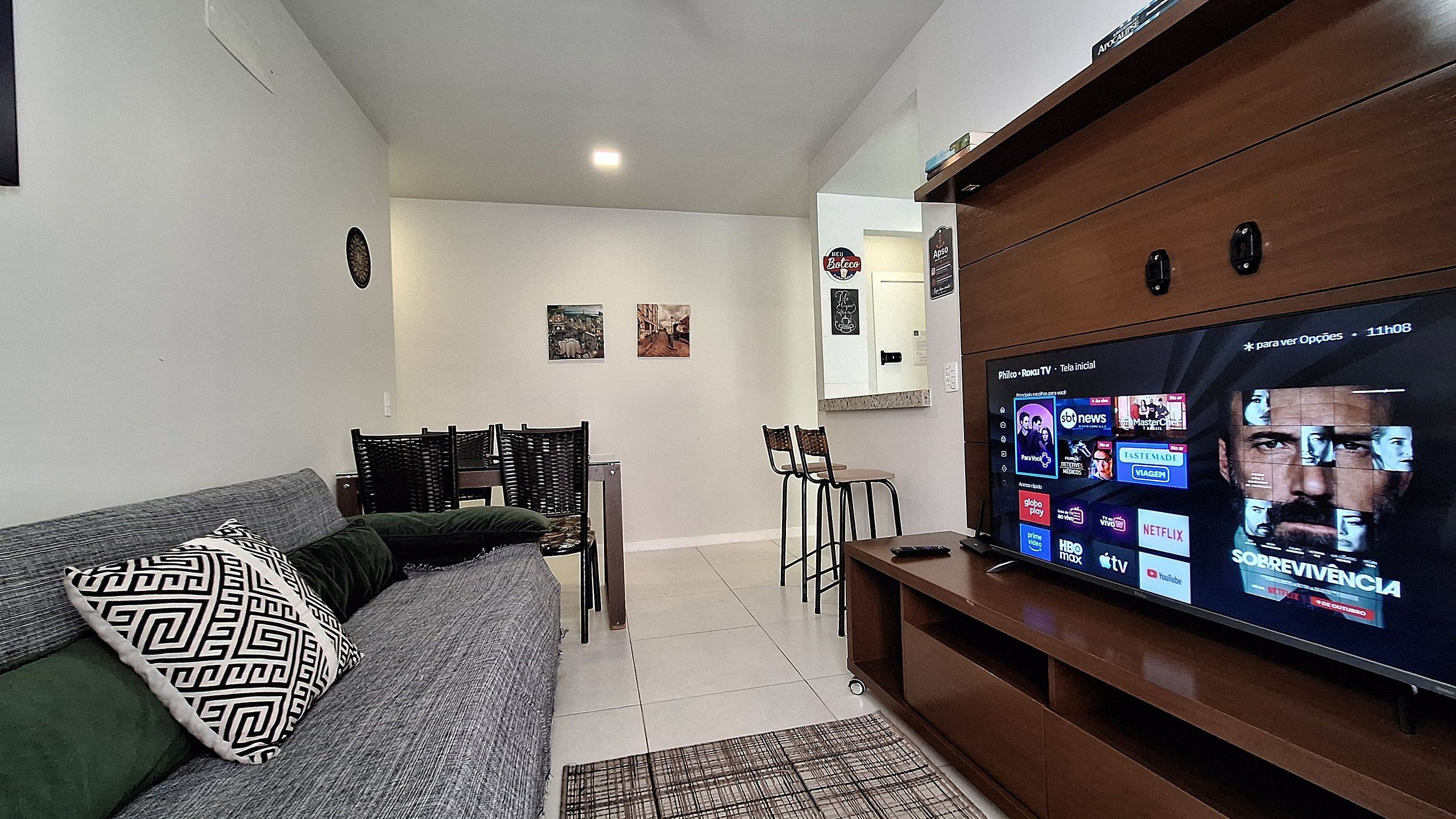 Uma sala de estar com sofá, mesa de centro, televisão e um espaço de jantar com cadeiras e mesa.