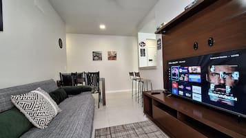 Uma sala de estar com sofá, mesa de centro, televisão e um espaço de jantar com cadeiras e mesa.
