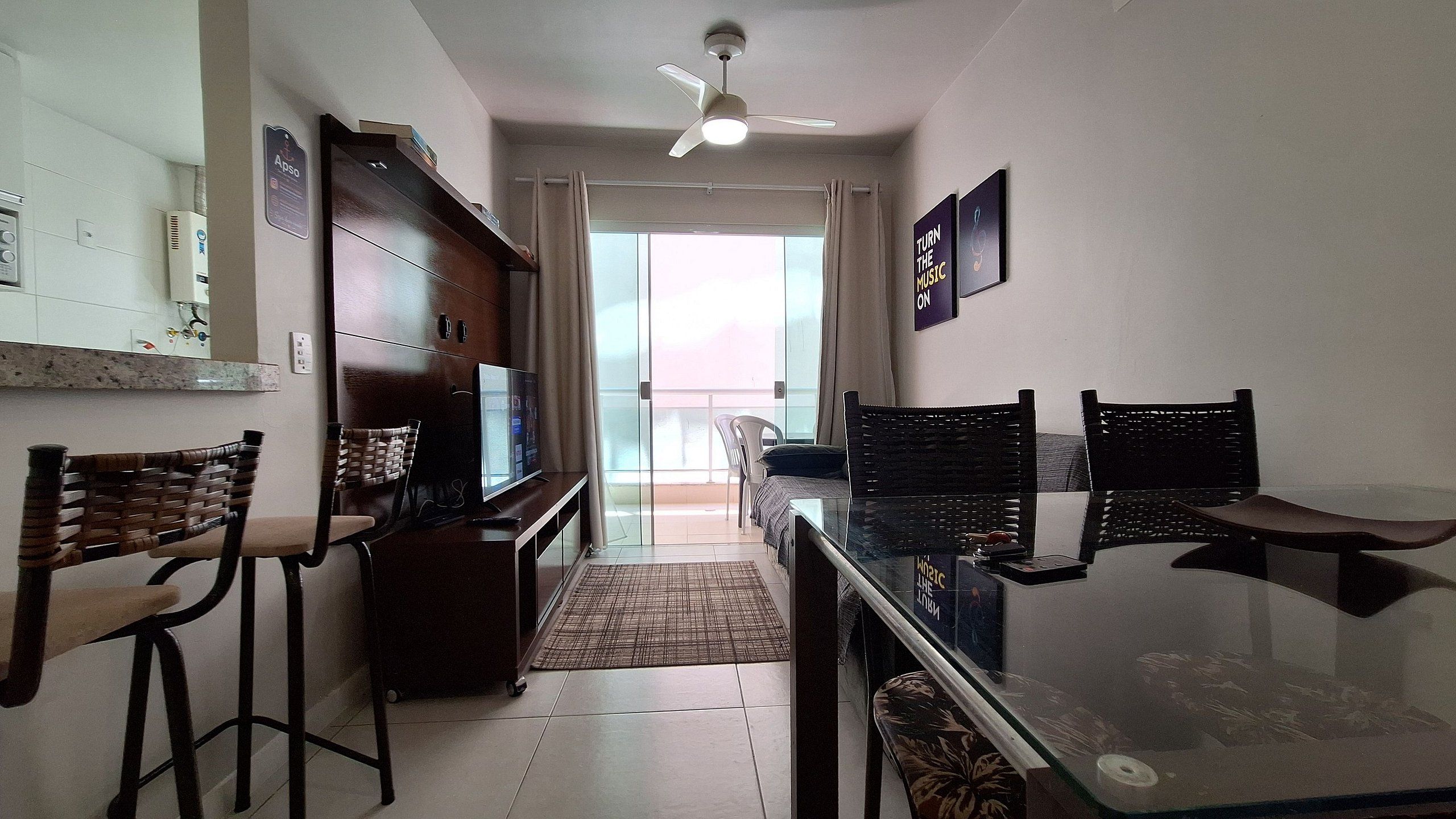 Uma sala de estar moderna com uma mesa de jantar de vidro, dois bancos altos, um sofá e um ventilador de teto.