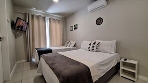 Une chambre d’hôtel avec deux lits, un téléviseur fixé au mur et un appareil de climatisation.