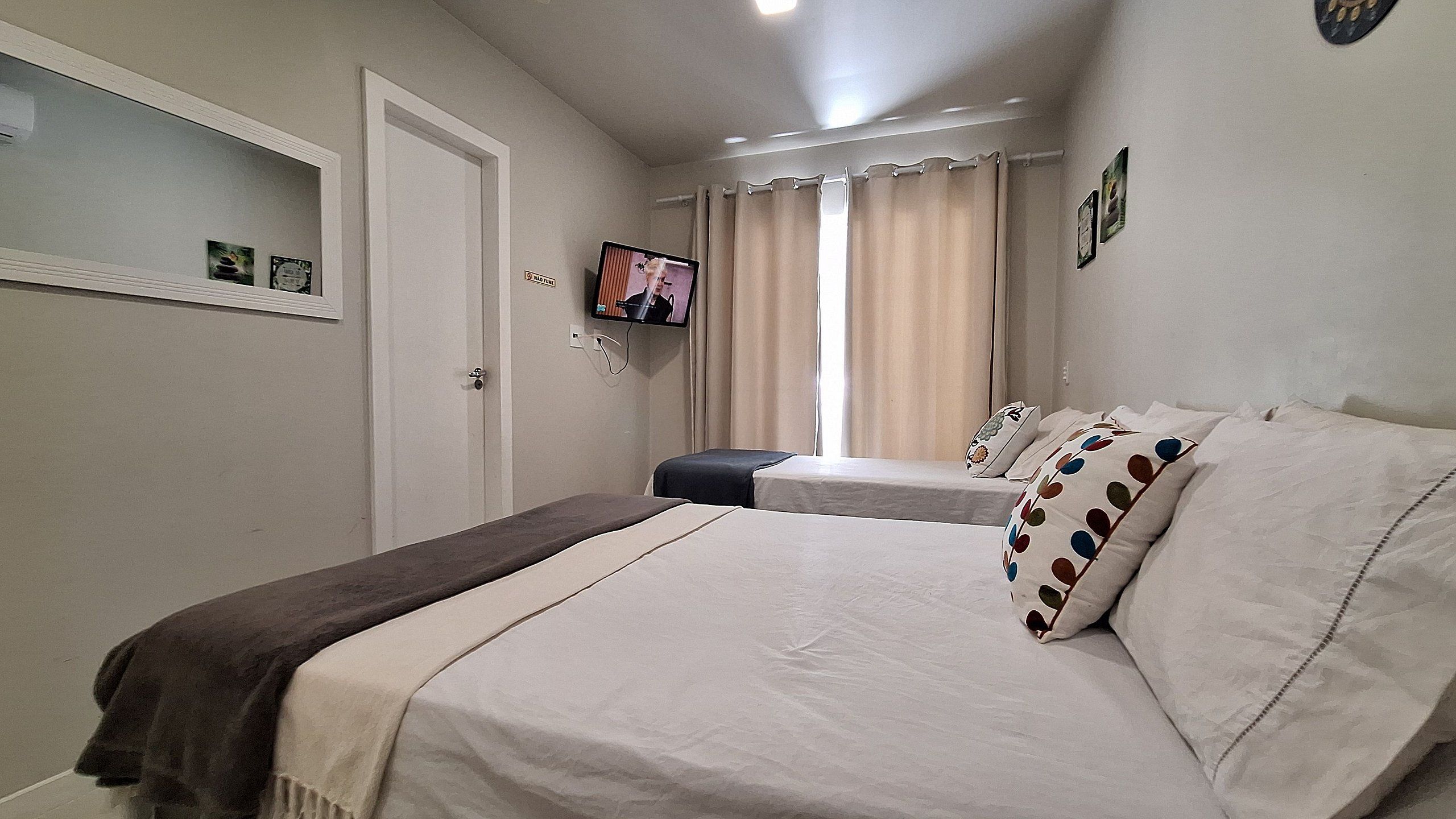 Un dormitori amb dos llits, una televisió penjada a la paret i una finestra amb cortines.