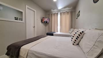 Een slaapkamer met twee bedden, een aan de muur bevestigde televisie en een raam met gordijnen.