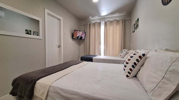 Une chambre avec deux lits, un téléviseur fixé au mur et une fenêtre avec des rideaux.