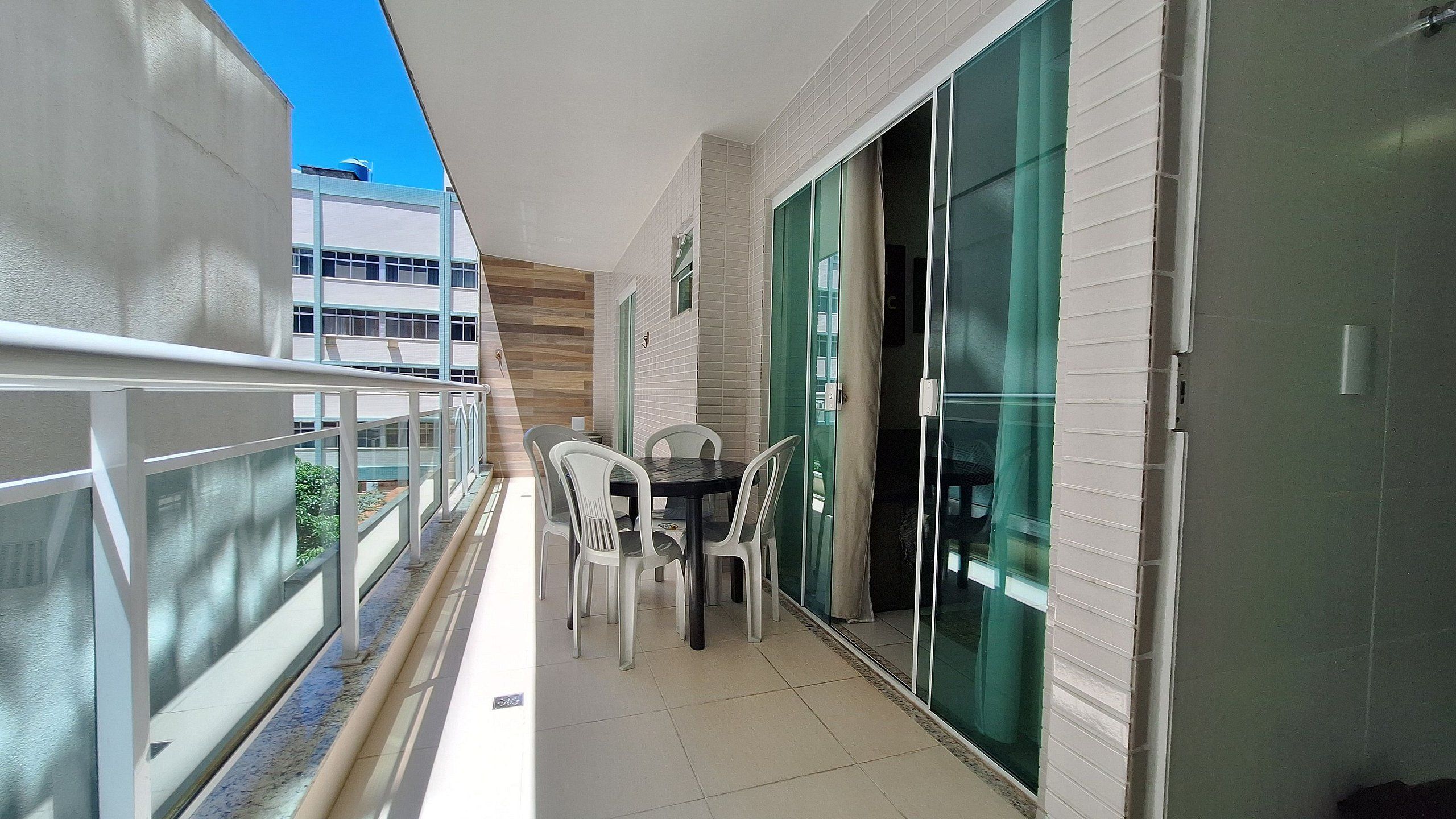 Varanda com mesa, cadeiras, porta de vidro e vista de um edifício.