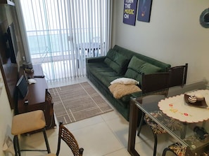 A living room with a green sofa, a glass dining table, and a view of the outside through large windows.