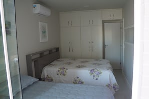A bedroom with two beds, a wardrobe, and an air conditioning unit.