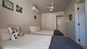 Quarto com duas camas, ventilador de teto, ar condicionado e guarda-roupa.