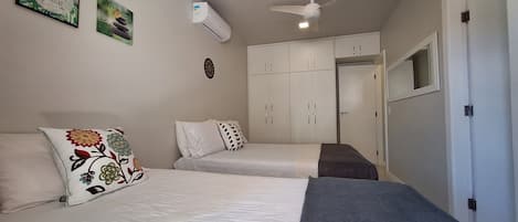 A bedroom with two beds, a ceiling fan, an air conditioning unit, and a wardrobe.