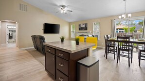 Una cocina moderna con una isla central, un comedor con un sofá amarillo y un ventilador de techo.