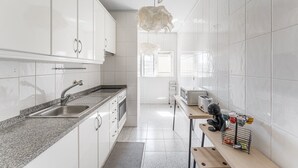A modern kitchen with white cabinets, a granite countertop, a stainless steel sink, and a hanging light fixture. - GuestReady - Modern apt near Matosinhos Beach (Matosinhos)