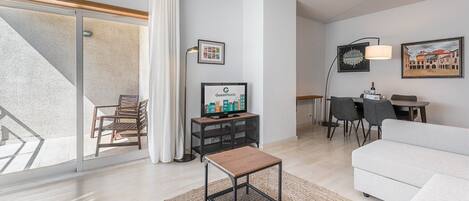 Ett modernt vardagsrum med en soffa, ett soffbord, en tv och en matplats med stolar och ett bord.