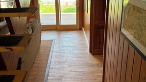 Interior de madera con un sofá, un banco de madera y una alfombra que conduce a un ventanal corredero.
