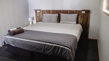 A hotel room with a large bed, a wooden headboard, a bedside table with a lamp, and a dark carpeted floor.