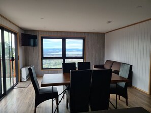 Una habitación moderna con un ventanal grande, un televisor de pantalla plana y una zona de comedor con sillas y una mesa.