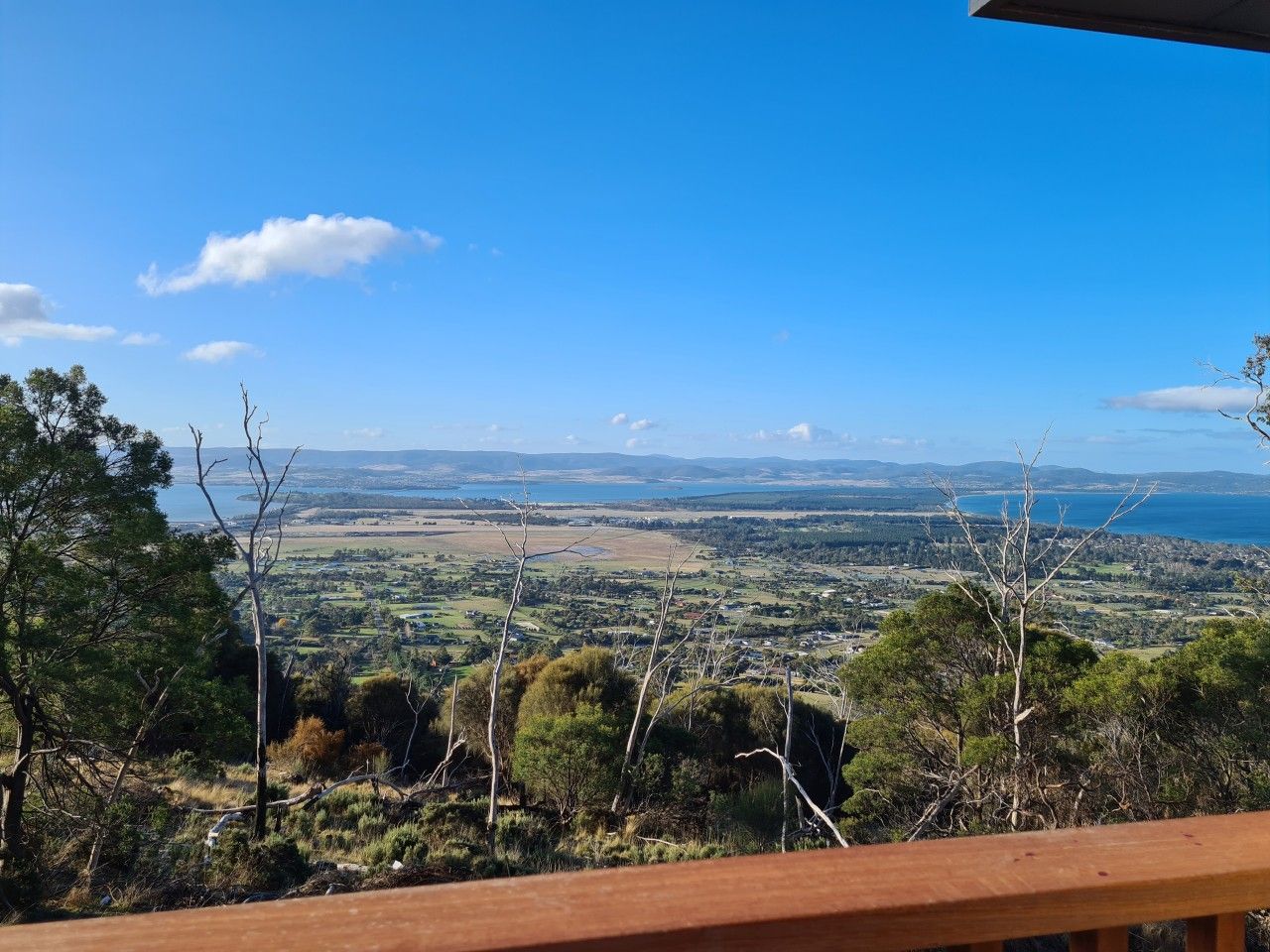 A view from a wooden deck overlooking a landscape with trees and a distant body of water.