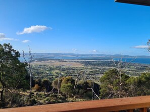 A view from a wooden deck overlooking a landscape with trees and a distant body of water.
