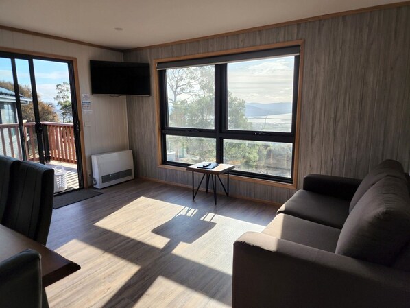 A modern living room with a large window, a flat-screen TV, and a small table.