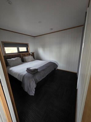 Een enkel bed met een houten hoofdbord, een raam met zonwering en een donkere vloer.