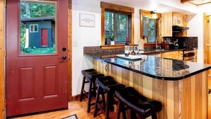 A kitchen with a wooden island, bar stools, and a red door. - Wild Goose Lodge | Hot Tub + Bunk Room (Glacier)