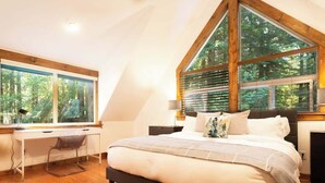 A bedroom with a large bed, a desk, and a window with a view of trees. - Wild Goose Lodge | Hot Tub + Bunk Room (Glacier)
