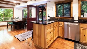 A kitchen with wooden cabinets, a stainless steel dishwasher, and a dining area with a table and chairs. - Wild Goose Lodge | Hot Tub + Bunk Room (Glacier)