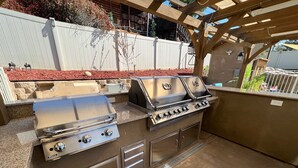 Ein Grill mit einer Steinarbeitsplatte und einer Pergola darüber.